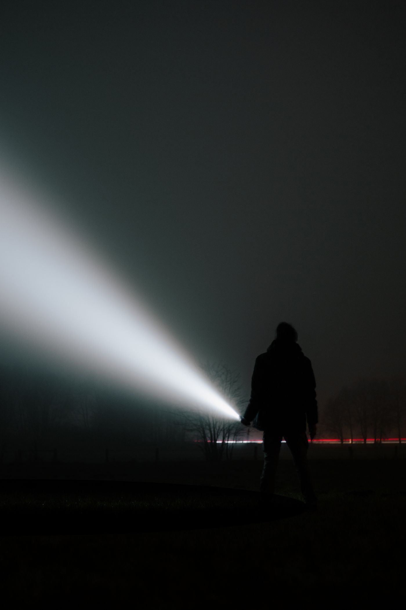 Silhouette of a person with a bright torch beam cutting through darkness and fog at night