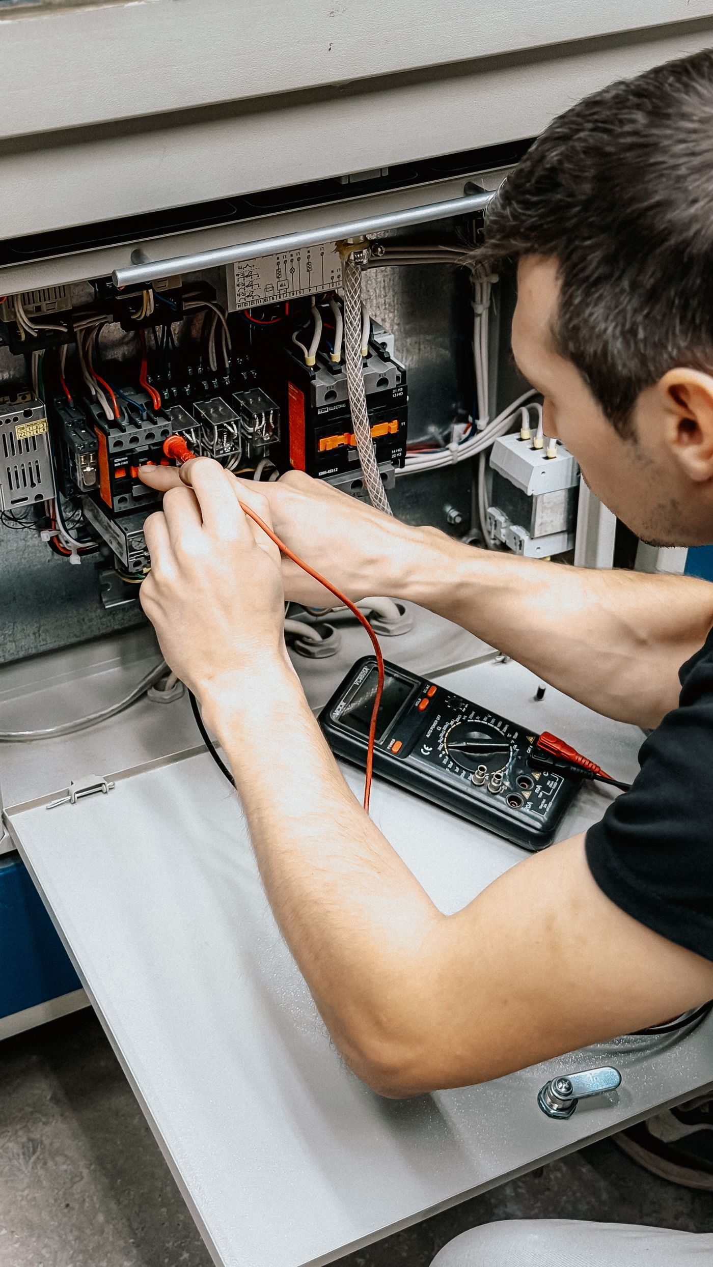 Electrician testing connections inside an open panel with a multimeter